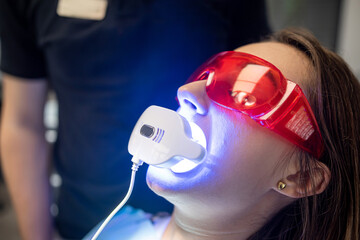 dentist with an assistant in overalls uses UV lamps during treatment of a patient's teeth.