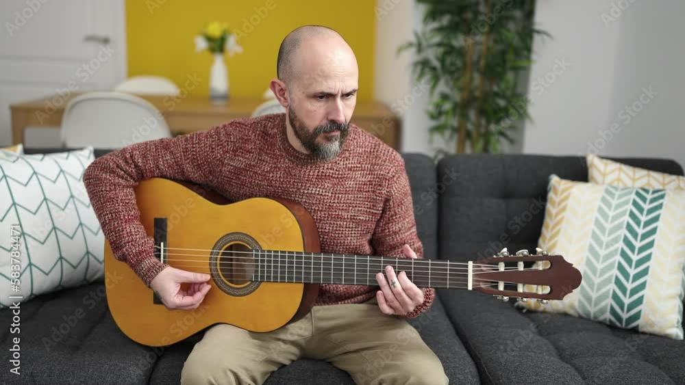 Canvas Prints Young bald man playing classical guitar sitting on sofa at home