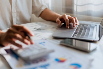 Close up of young man using calculator and laptop for doing financial mathematics on wooden table in office and working background - business, tax, accounting, statistics and analytical research conce