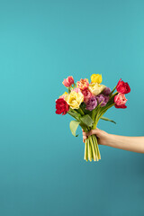 Banner. A woman's hand holds a beautiful bouquet of tulips against a blue wall. Greeting card for March 8 and International Women's Day. The concept of congratulations and celebration.