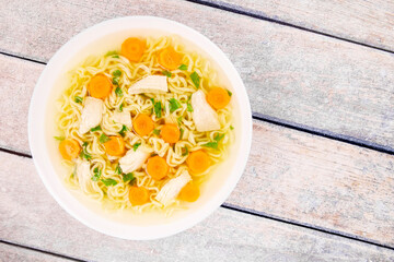 Homemade chicken soup with noodles and vegetables in a white bowl, on a wooden background.