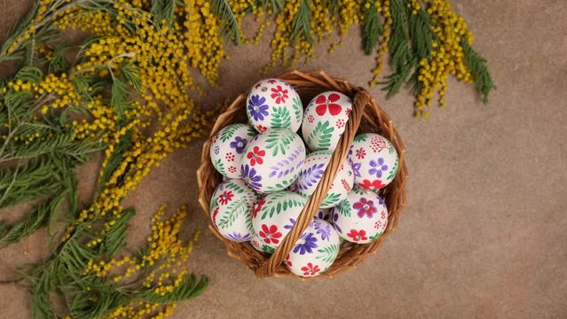 Colorful Easter eggs - traditional symbol for religious holiday. Easter eggs in the basket and mimosa flowers rotation. Happy holiday concept background  flat lay top view slow motion vertical 