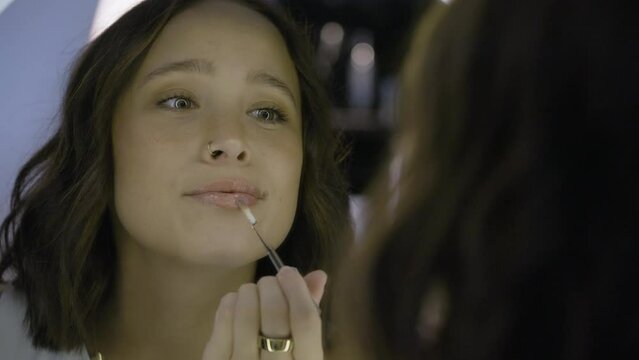 Slow motion shot of an attractive female applying lipgloss in a vanity mirror