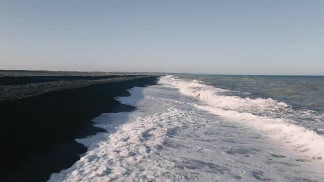 Extremely low, fast flight over big waves crashing onto black rocky beach