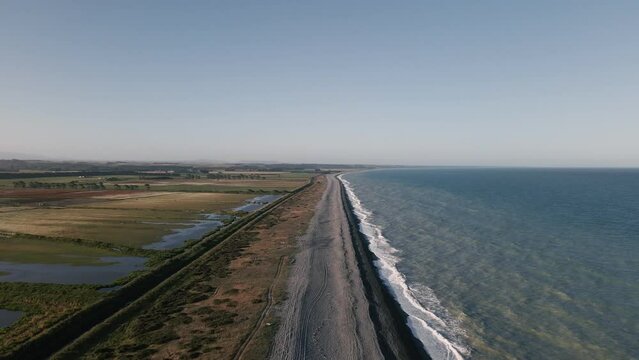 Aerial establishing shot of long empty black sand beach during golden hour