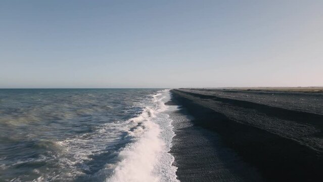 Epic low flight over big waves crashing onto black rocky beach at golden hour