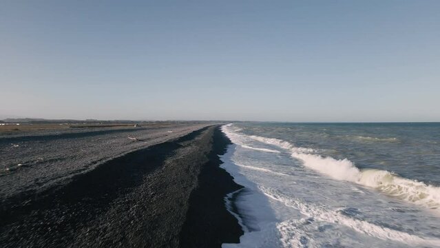 Low fast flight over strong waves that crash onto black rocky beach in golden hour light