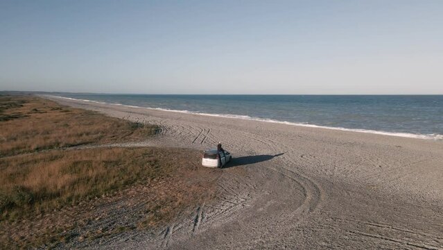 person sitting on van watching a splendid sunset right at the beach; aerial orbiting view