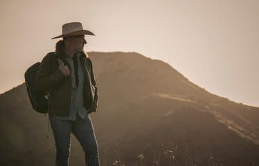 Adult man on cowboy hat standing on hill against mountain during sunrise