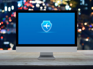 Airplane with shield flat icon on desktop modern computer monitor screen on wooden table over blur colorful night light traffic jam road in city, Business travel insurance and safety online concept