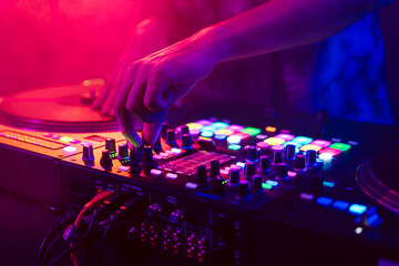 Close up of DJ hands on dj console mixer during concert in the club