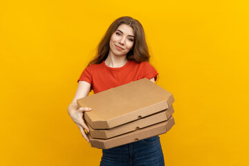 On a bright yellow backdrop, a woman downing a crimson T-shirt of a pizza delivery service clutches some pizza boxes tightly, ready to make a delivery