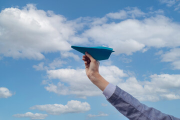 hand holding origami paper airplane against blue sky, concept of freedom, freelancing, travel