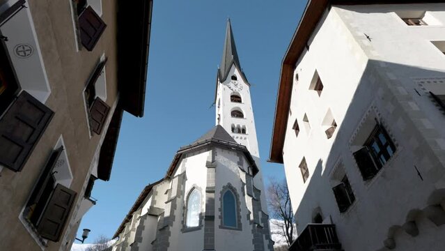 View of a traditional Swiss village church on a sunny winter day in Zuoz, Switzerland.