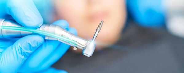 Closeup photo of dental implant in dentist hands with female patient in dental chair behind.