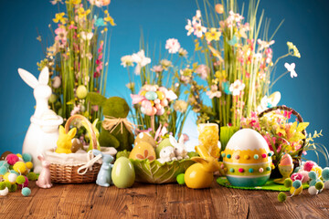 Fototapeta na wymiar Easter theme. Easter decorations. Easter eggs in basket and easter bunny. Bouquet of spring flowers. Rustic brown table and blue background.