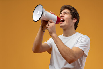 Young man shouting into megaphone making announcement against yellow background