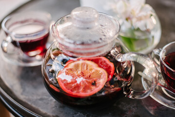 Street cafe in the morning, on the table there are two glass glasses and fruit tea with a floating slice of orange is poured in a transparent glass teapot. Blurred background and foreground.