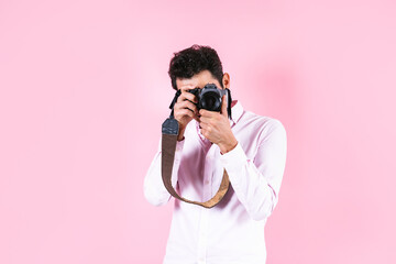 portrait of young hispanic man using a camera to take photos on pink background in Mexico Latin America	