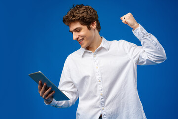 Happy young man using digital tablet on blue background.