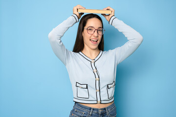 Photo of smiling shiny toothy clever lady holding a book over head isolated over blue background.