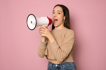 Young smiling woman isolated on pink background shouting through a megaphone to announce something