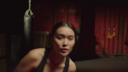 Portrait of determined concentrated sporty fit attractive Asian female boxer in boxing gloves shadowboxing, training, and improving punching techniques, throwing uppercut and jab in gym.