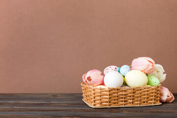 Happy Easter composition. Easter eggs in basket on colored table with yellow Tulips. Natural dyed colorful eggs background with copy space