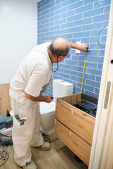 Senior mason measuring with a measure tape to install new bathroom furniture.