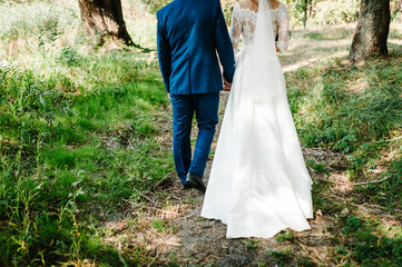 Wedding couple are walking their backs in the forest and admire nature. Wedding ceremony and photo shoot outdoors. Newlyweds. Down view.