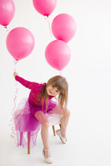 Cute happy child girl 4-5 year old wear princess dress posing with balloons having birthday party over white in room. Childhood.