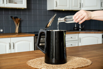 Woman pouring natural destilled acid white vinegar in electric kettle to remove boil away the...