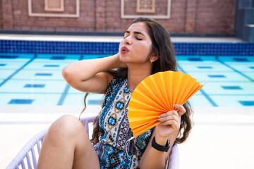 Indian woman using a paper hand waver fan suffering from hot summer weather or high temperature,...