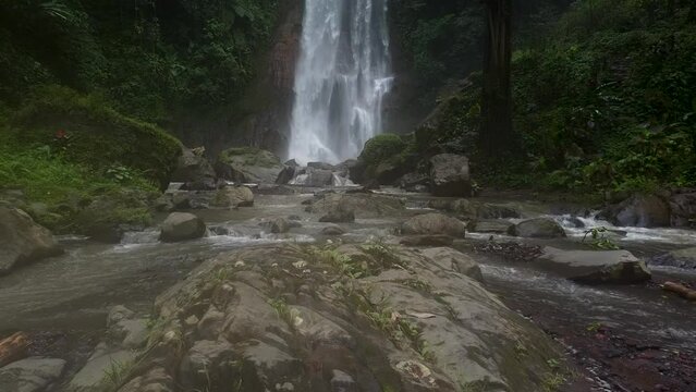 Aerial backwards shot of Gitgit Waterfall with rocky stream in jungle of Bali