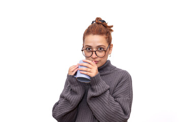 Mujer joven, con una taza de café, y abrigo, en un fondo blanco.