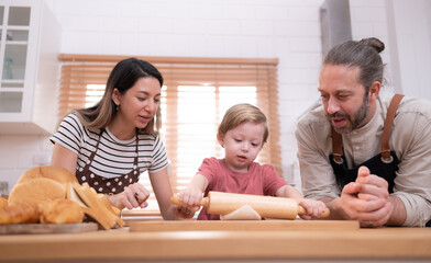 Mom and dad in the kitchen of the house with their small children. Have a good time baking bread and making dinner together.