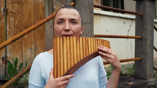 A young woman playing a pan flute near an old house