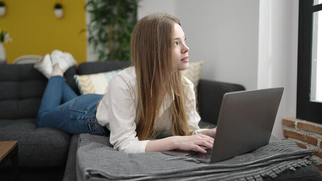 Young blonde woman using laptop lying on sofa at home
