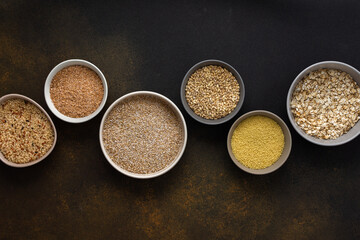 Fototapeta na wymiar Various grain cereals in bowls, top view on a brown background with bowls of cereals