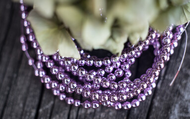 The photo shows hematite beads. This is a natural stone painted in different colors, round and hexagonal. Placed on a wooden board on a background of dried hydrangeas.