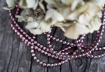 The photo shows hematite beads. This is a natural stone painted in different colors, round and hexagonal. Placed on a wooden board on a background of dried hydrangeas.