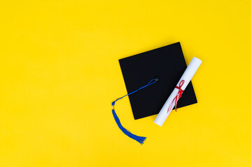 Graduation cap and diploma on yellow background