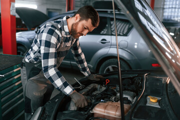 Naklejka premium In gloves. Repairing car. Man in uniform is working in the auto salon
