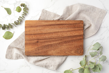Fototapeta na wymiar Wood cutting board on linen napkin with leaves on marble background