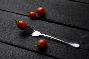 A fork with a tomato on it on a black table.