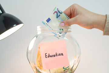 Putting euro money into glass jar with Education inscription. Concept of saving up for education in...