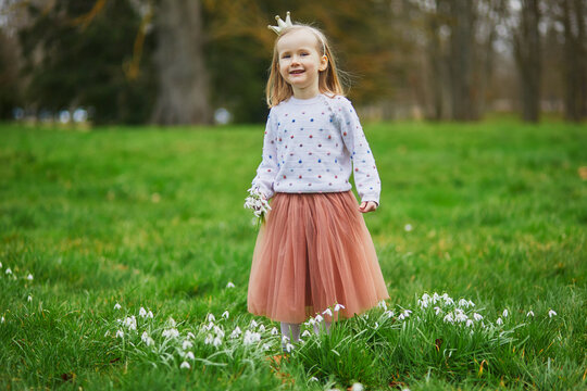 Cute preschooler girl in princess crown standing in the grass with many snowdrop flowers