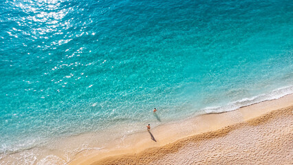 Aerial view of couple standing in beautiful sandy beach with soft turquoise ocean wave. Tropical...