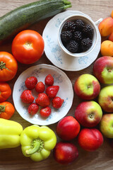 Berries in vintage porcelain dishes, other healthy fruit and vegetable on wooden table. Top view.