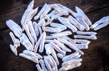 Natural freshwater pearls of various shapes and colors are photographed on a wooden board and a piece of leather.